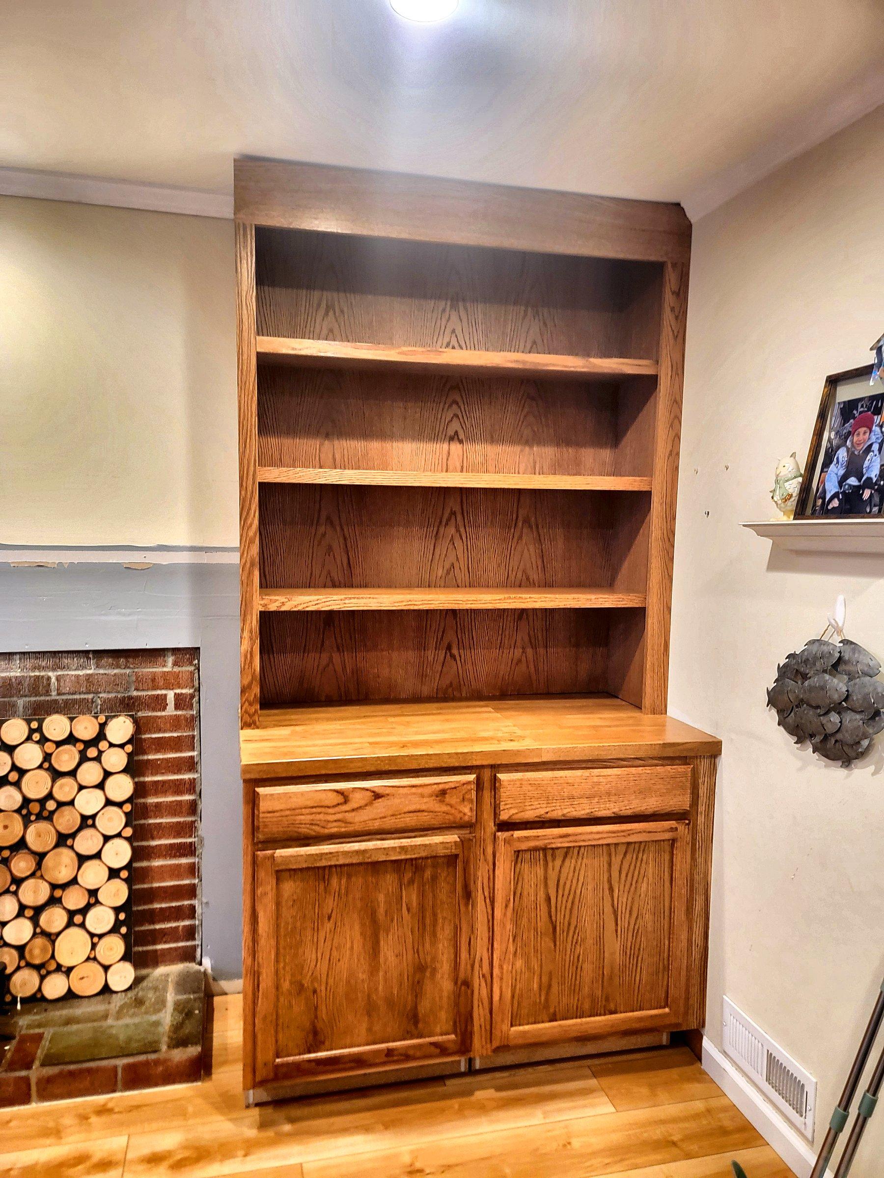 A stained wood hutch with open shelves, beside a stone fireplace.