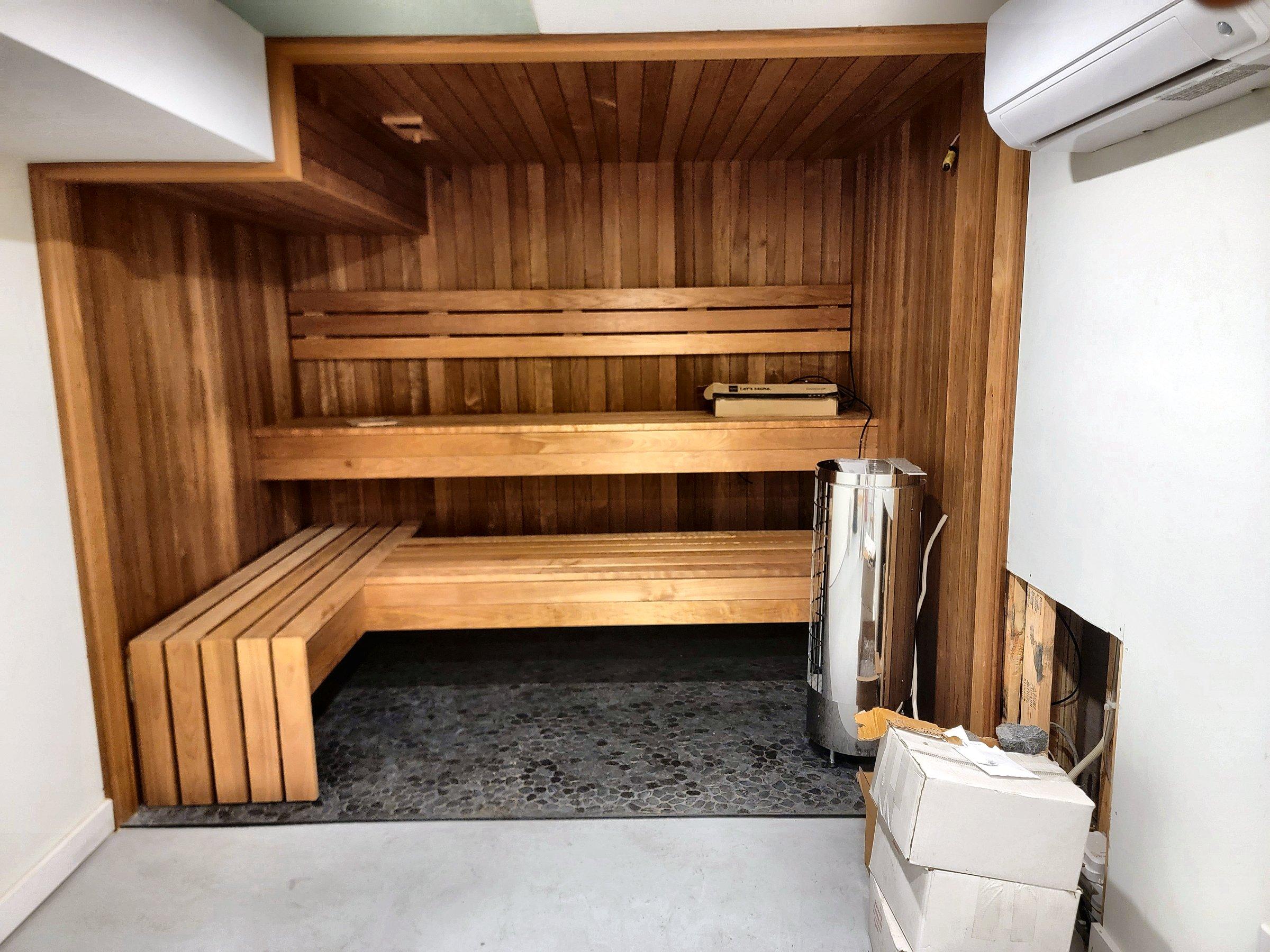 A cedar sauna with benches along the wall, a glass door, and a heater.